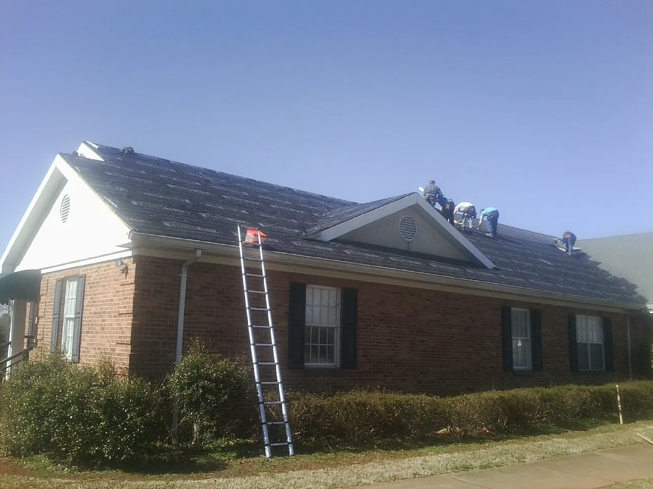 Crew tearing shingles off a brick ranch roof with a ladder set — Metal Roof Repair work by our crew in Glencliff