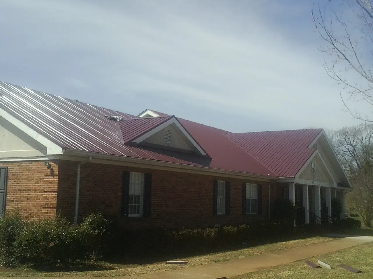 Red metal roof with gabled entries on a long brick building, from a Hail Damage Roof Repair job in Glencliff