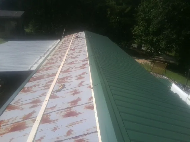 Old rusted panels beside newly installed green metal roofing — Wind Damage Roof Repair by Roofing Brothers in Glencliff