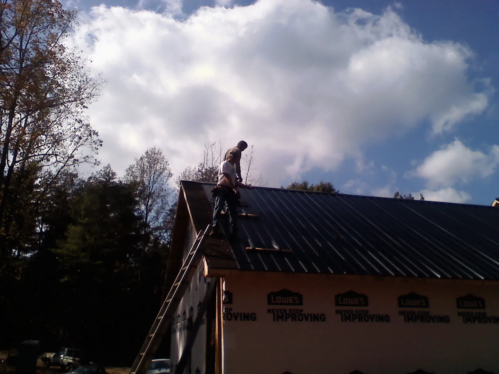 Roofer fastening dark metal panels high against a cloudy sky, from a Roof Inspection job in Glencliff