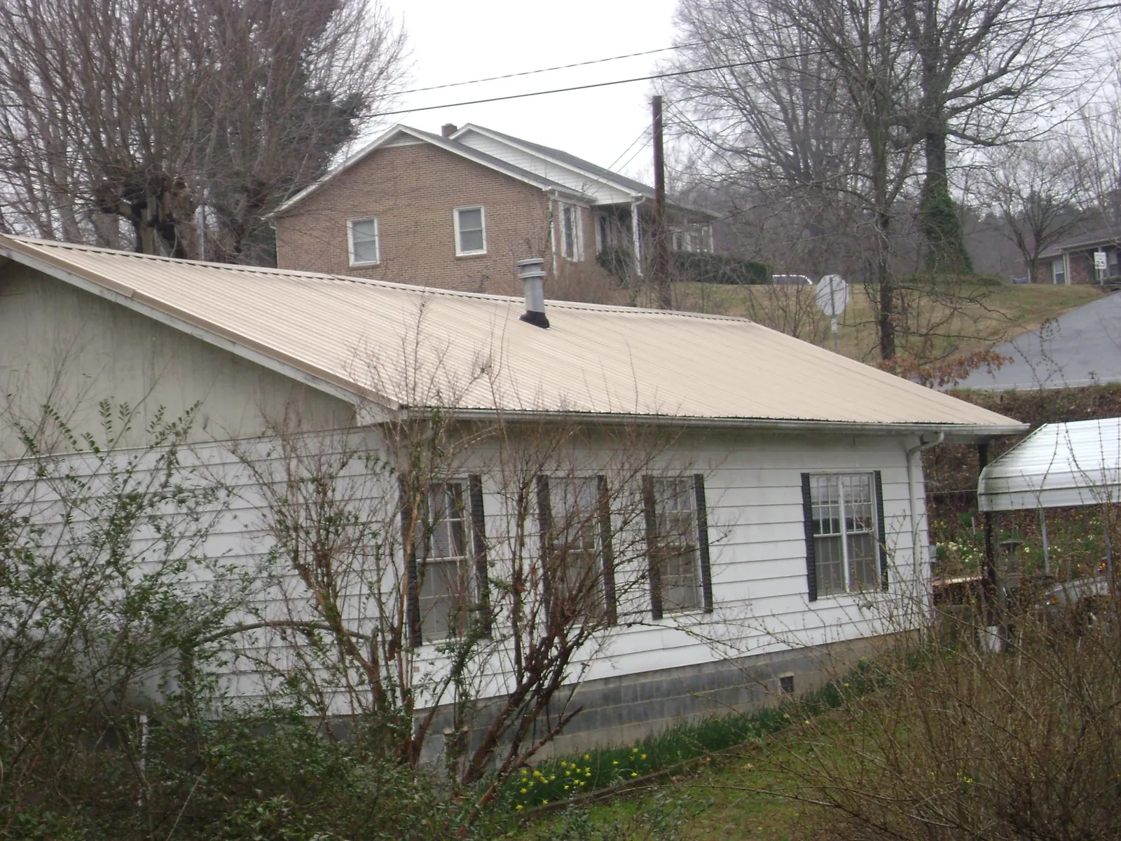 Tan metal roof on a white sided house set into a hillside — Commercial Roofing by Roofing Brothers in Glencliff