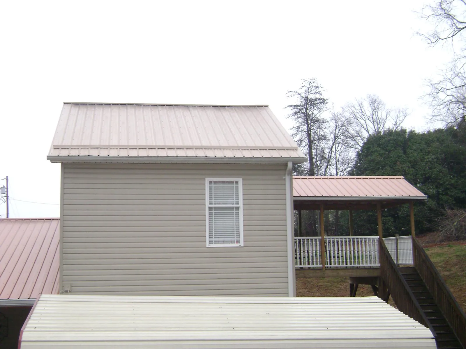 Tan metal roofs on a two story addition and attached porch, from a Roof Replacement job in Glencliff